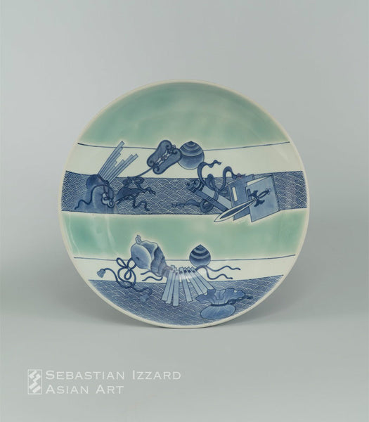 SERVING DISH (<i>SHAKUZARA</i>) WITH THE ATTRIBUTES OF THE SEVEN GODS OF GOOD FORTUNE (<i>TAKARAMONO</i>)<br>Hizen ware, <i>Nabeshima type </i>: porcelain with underglaze blue and celadon Japan, Edo period, circa 1680 D. 12⅞ in. (32.8 cm)