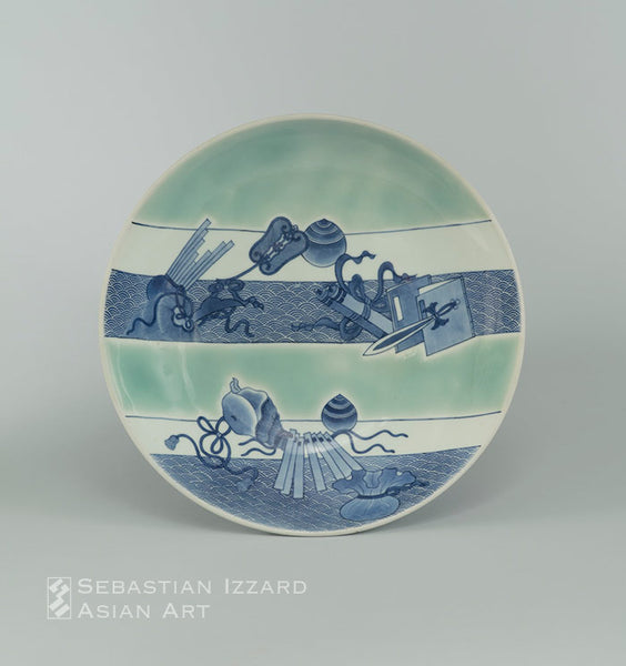 SERVING DISH (SHAKUZARA) WITH THE ATTRIBUTES OF THE SEVEN GODS OF GOOD FORTUNE (TAKARAMONO)  Hizen ware, Nabeshima type: porcelain with underglaze blue and celadon  Edo period, circa 1680 Diameter 12⅞ in. (32.8 cm) 